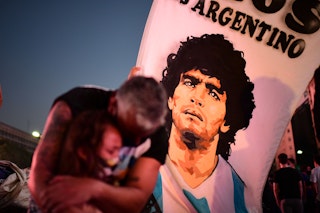 TOPSHOT - A father and her daughter, fans of Argentinian football legend Diego Maradona, mourn as they gather by the Obelisk to pay homage on the day of his death in Buenos Aires, on November 25, 2020. - The body of Argentine football legend Diego Maradona, who died earlier today, will lie in state at the presidential palace in Buenos Aires during three days of national mourning, the presidency announced. (Photo by RONALDO SCHEMIDT / AFP) (Photo by RONALDO SCHEMIDT/AFP via Getty Images)